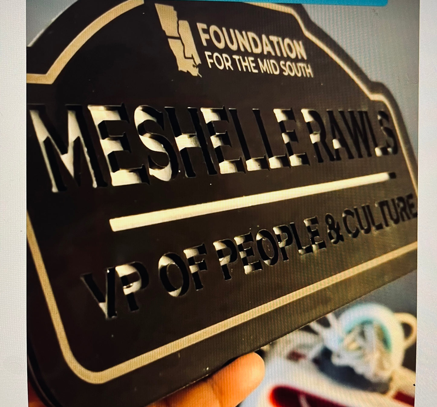 Metallic nameplate with engraved text and logo, held by a hand.