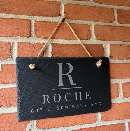 Slate sign with 'Roche' and address hanging on a brick wall