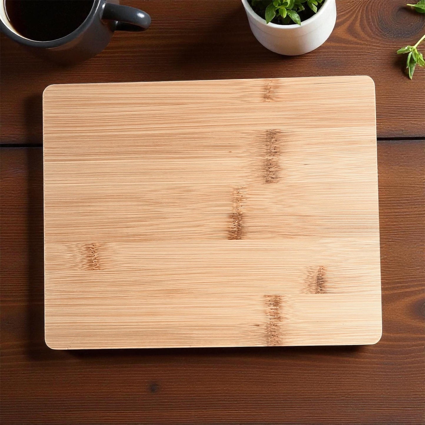 Wooden cutting board on a wooden surface with a cup and plant in the background
