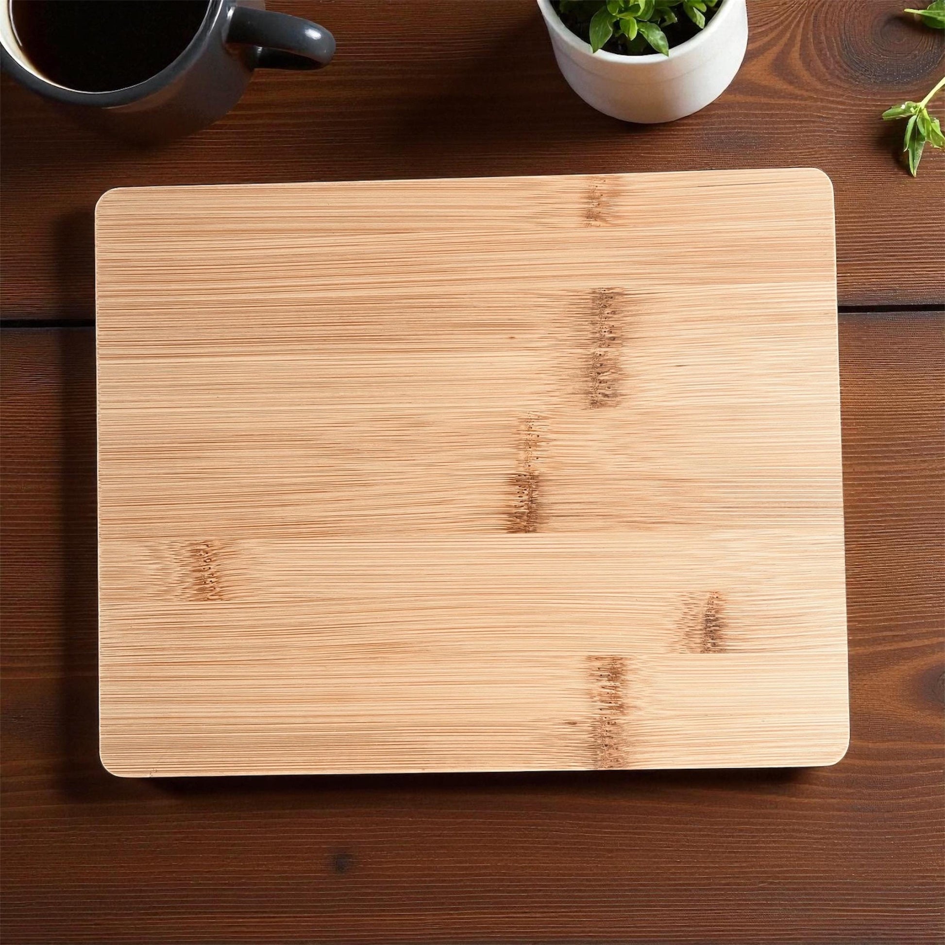 Wooden cutting board on a wooden surface with a cup and plant in the background