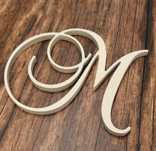 A single decorative cursive monogram letter N in a light natural wood finish, displayed on a dark brown wood grain surface.
