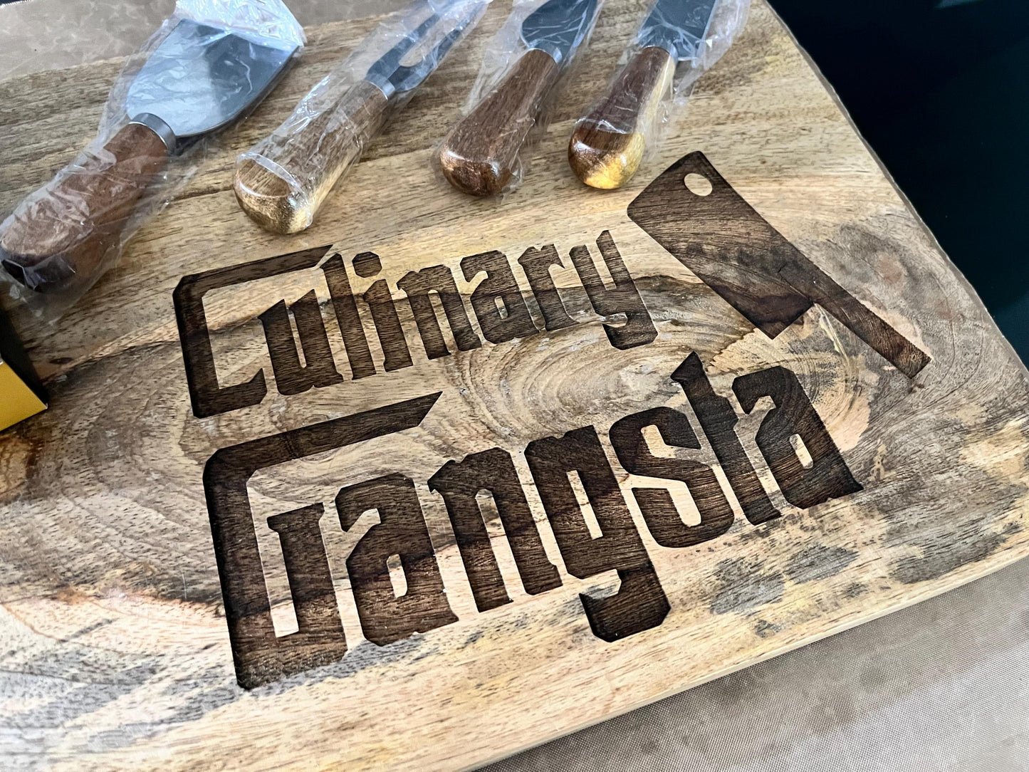 Wooden cutting board with 'Culinary Gangsta' engraving and kitchen knives.